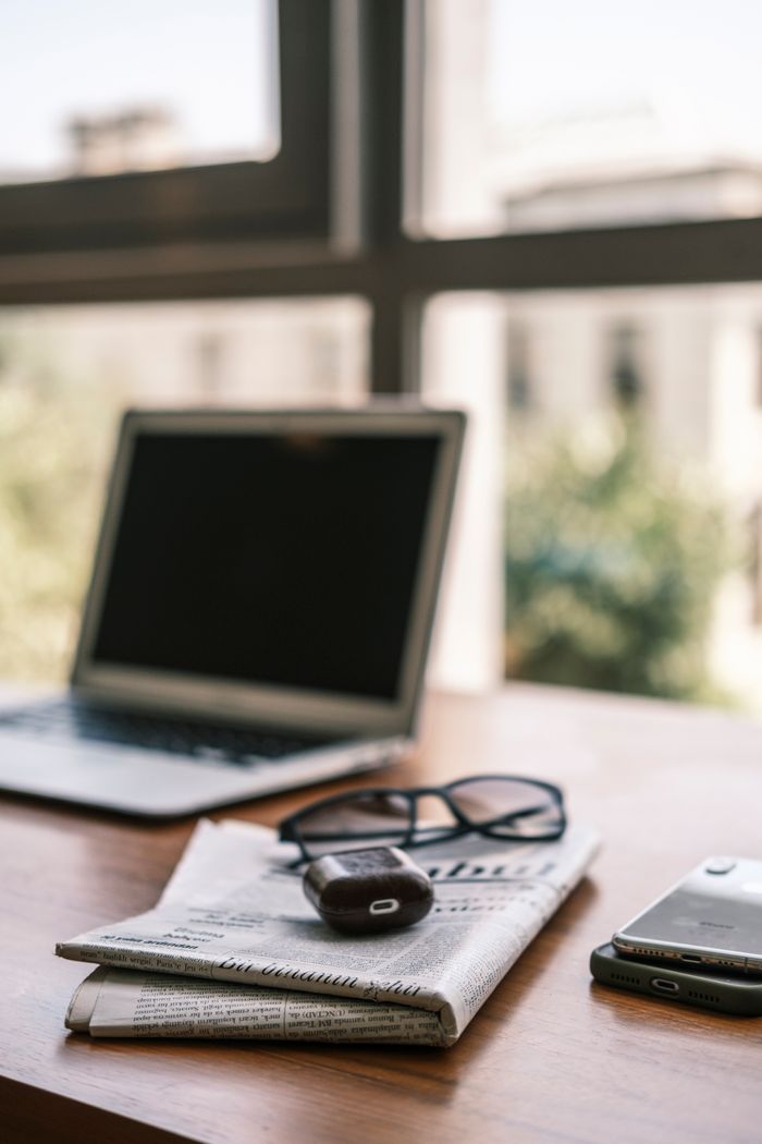 A close-up of a desk setup with a laptop, smartphone, and newspaper, perfect for business themes.